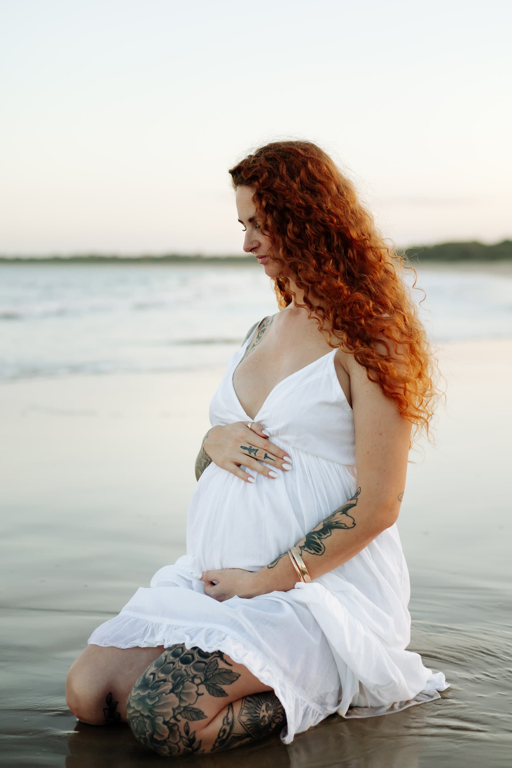 Silhouette of a pregnant woman against a glowing ocean horizon captured at sunset during a Mackay maternity shoot.