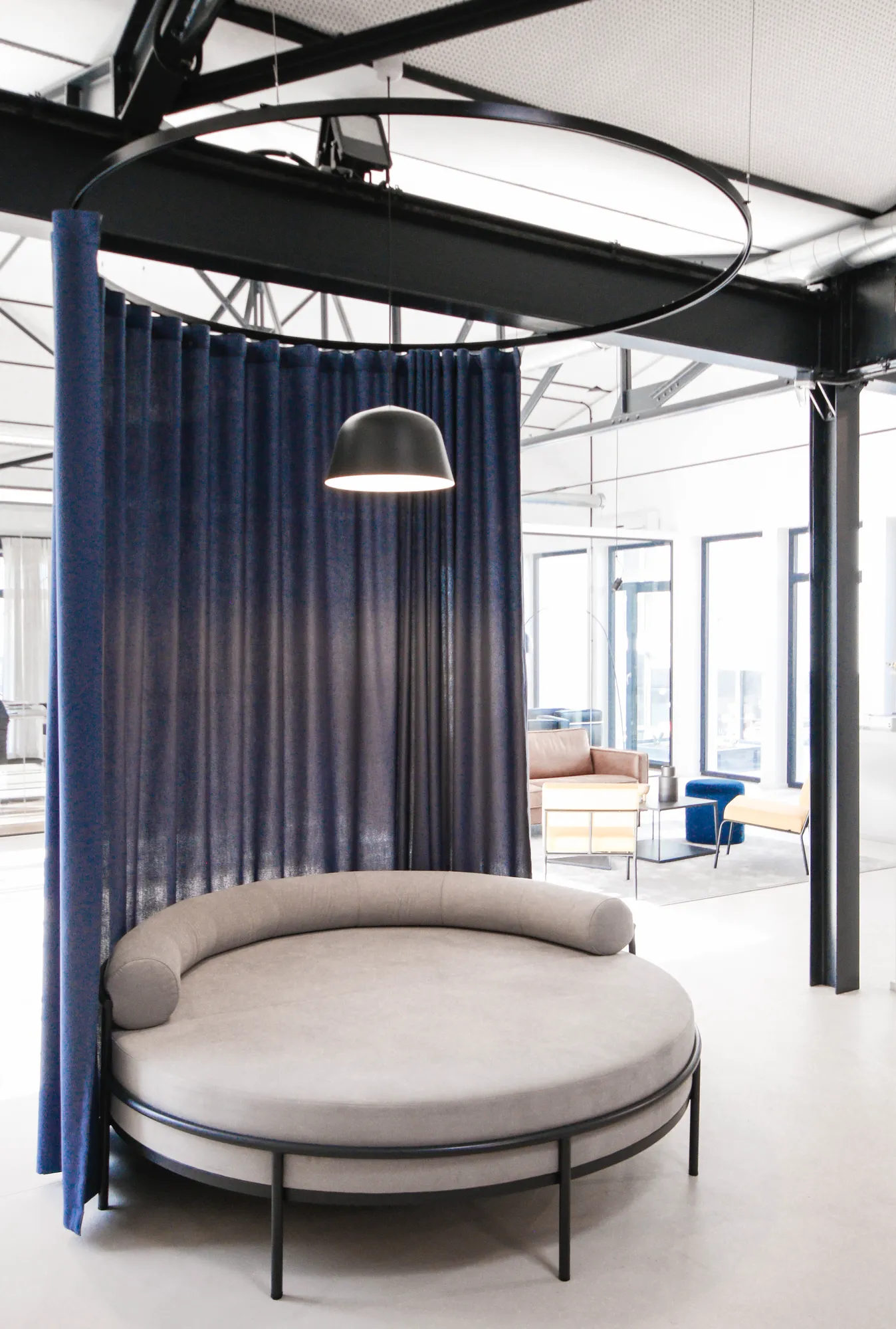 Round grey daybed behind a blue curtain ring with pendant light in the loft.