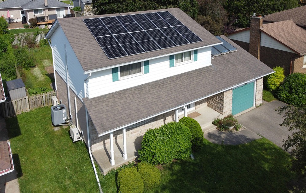 Aerial view of a modern house with solar panels on the roof, surrounded by greenery and a lawn.