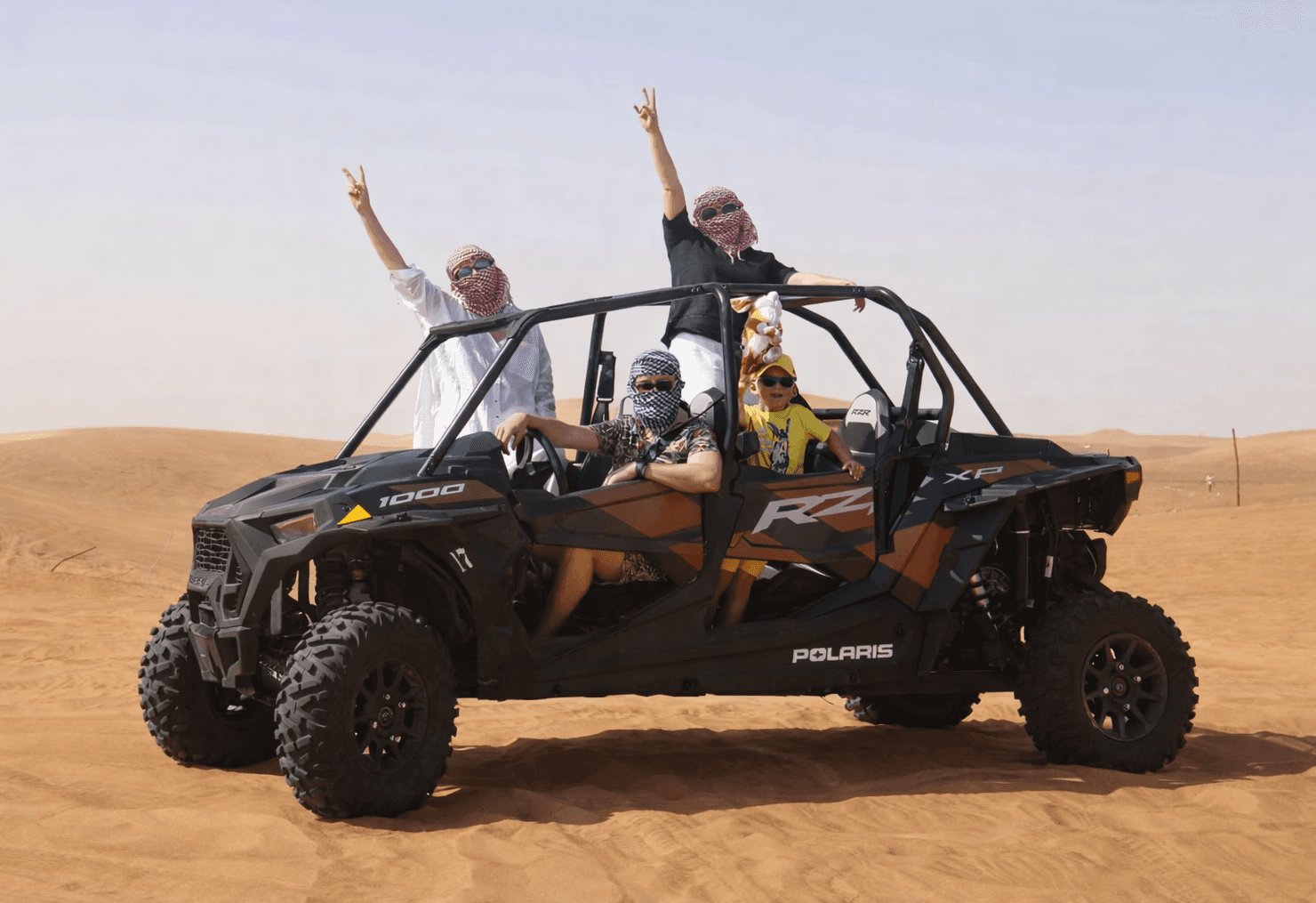 A family posing for a photo in a 4-seater Polaris RZR 1000cc buggy during a dune bashing tour in the Dubai desert with Dune Quest Tours