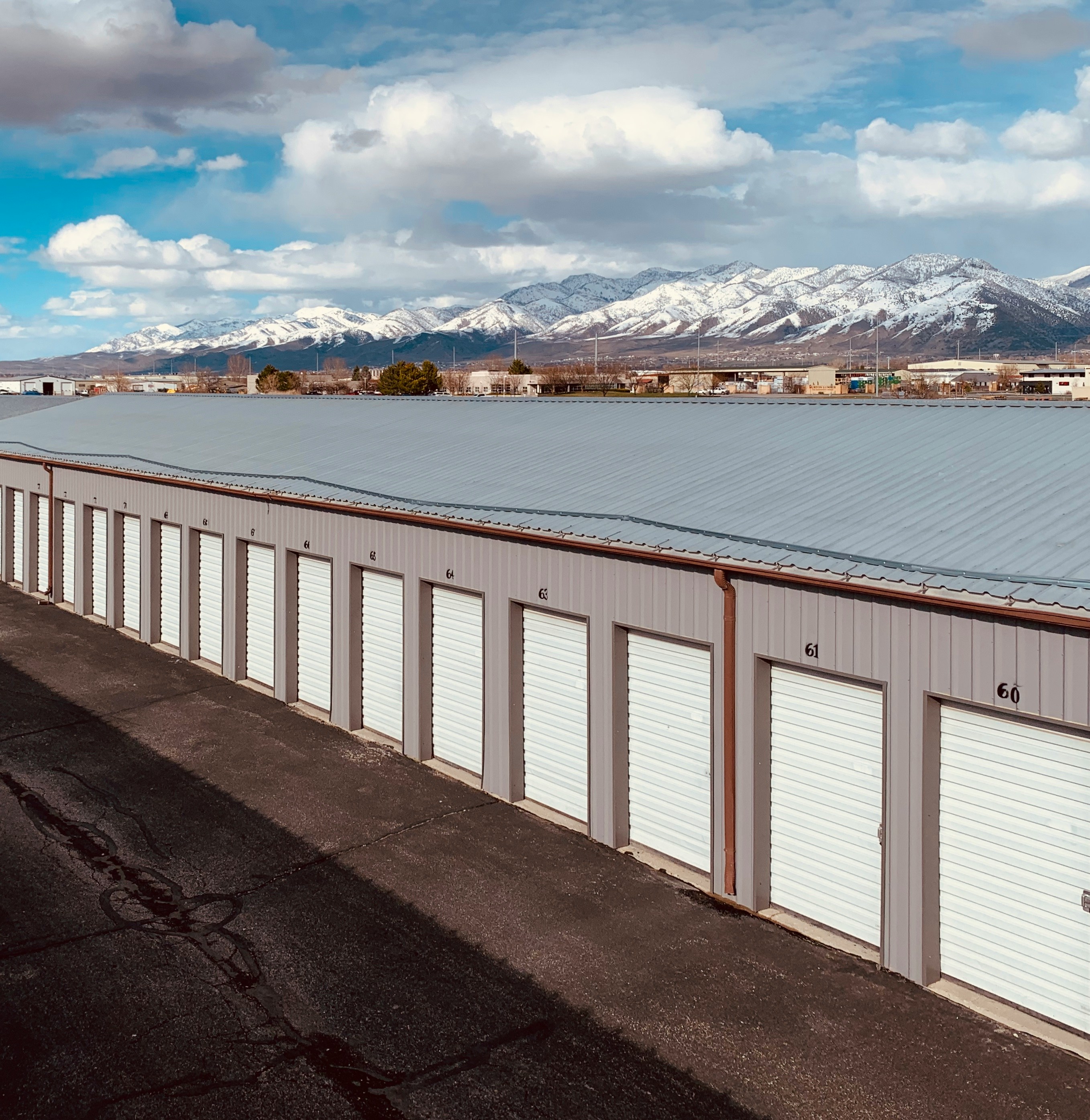 Enterprise Self Storage facility with rows of white roll-up storage unit doors and snow-capped mountains in the background.
