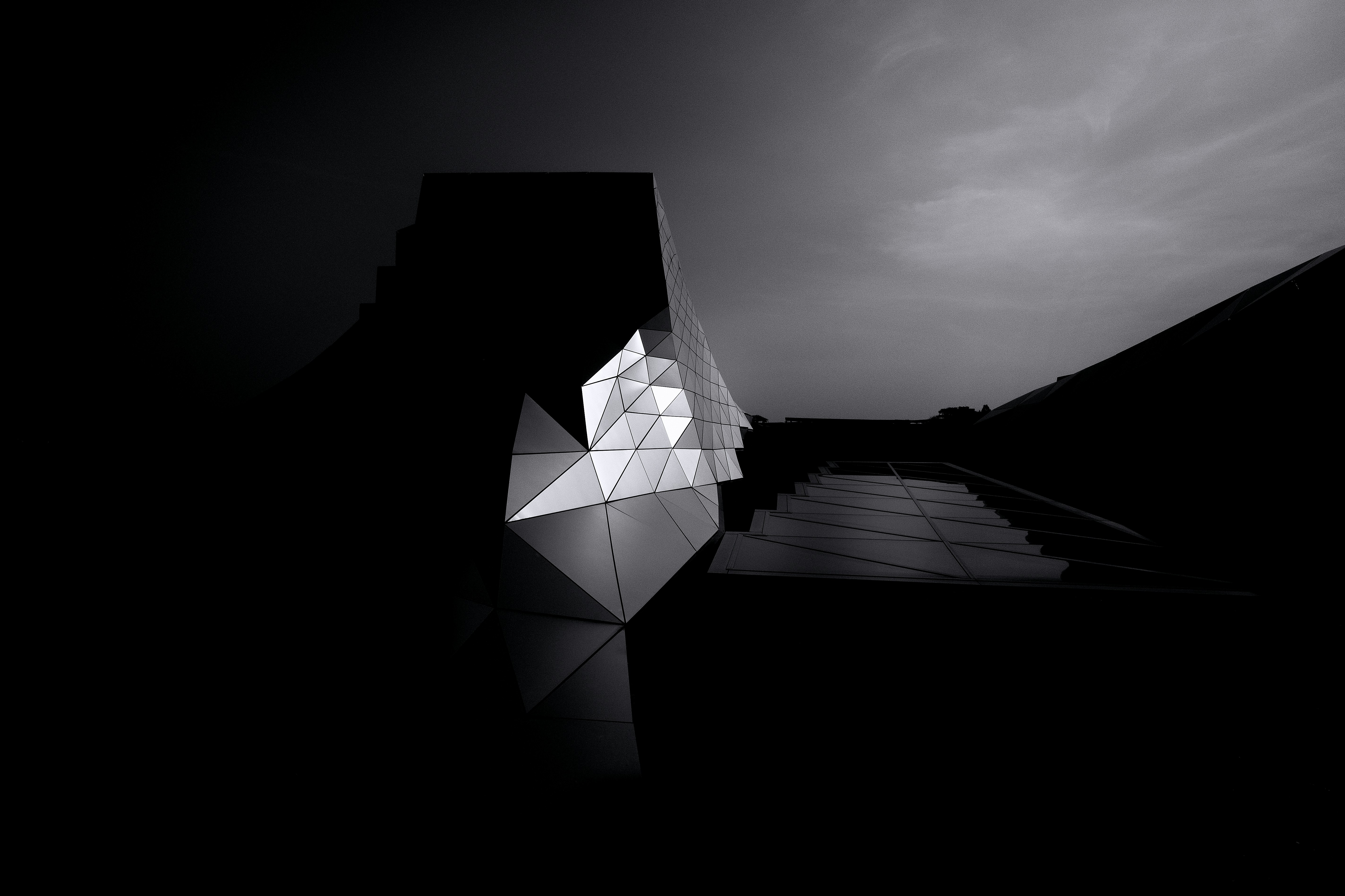 A man in a brown blazer and a woman in a light sweater sit at a desk with a laptop, discussing something. The room is dimly lit, creating a focused atmosphere.