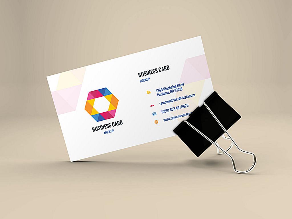 A business card with a modern geometric logo and contact details clipped with a black binder clip, displayed on a neutral background.