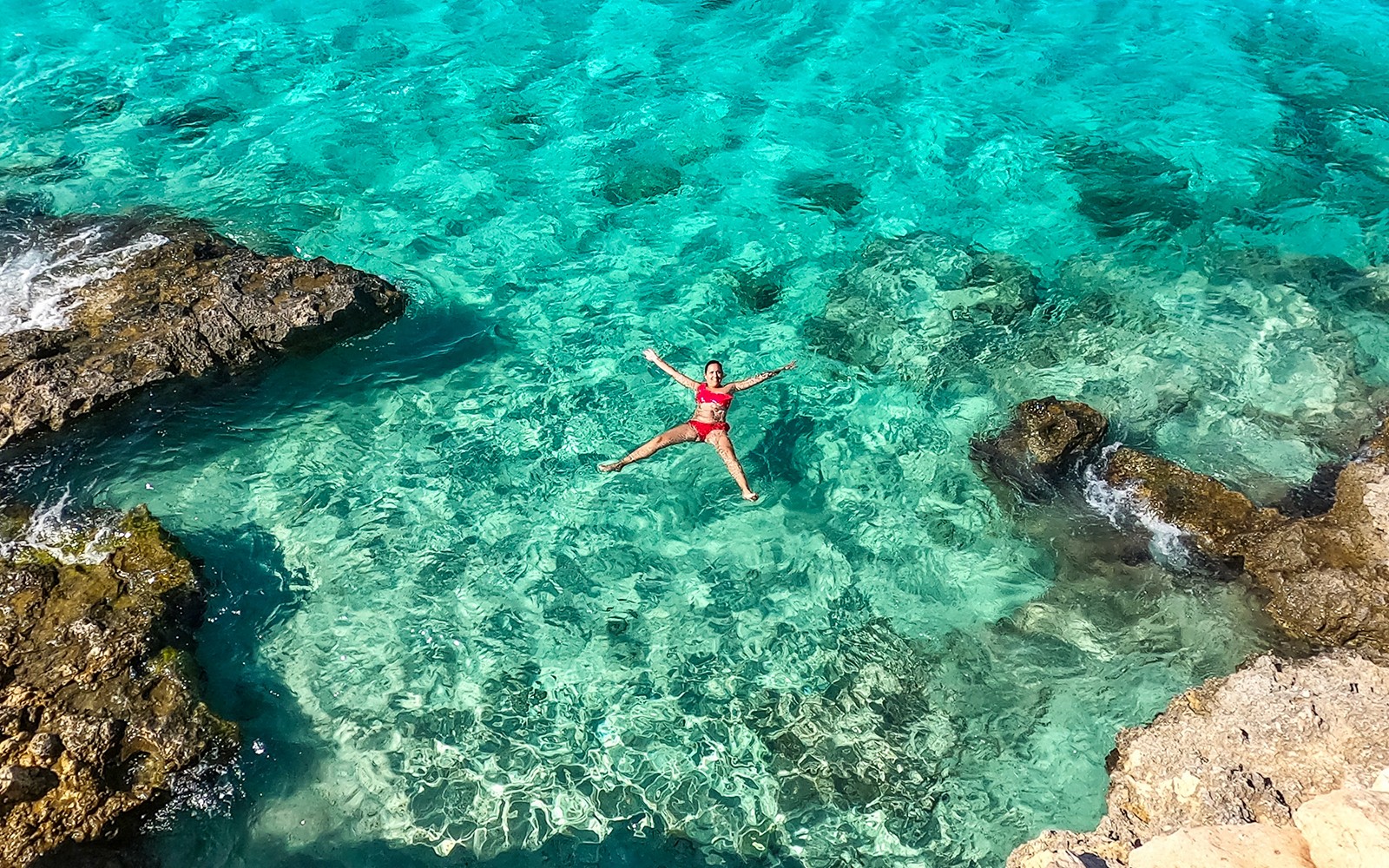 Person floating in clear turquoise water near rocky shore, Gozo and Comino cruise.