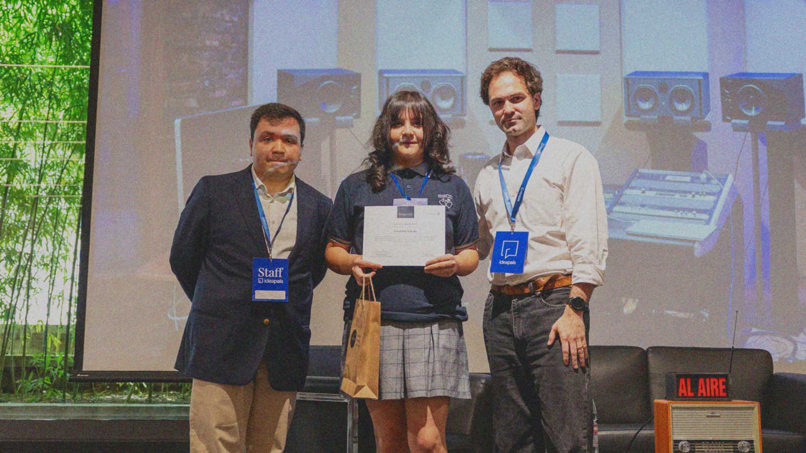 Foto de dos miembros del equipo de IdeaPaís con una estudiante que recibió el máximo reconocimiento en la primera edición del concurso Semilla