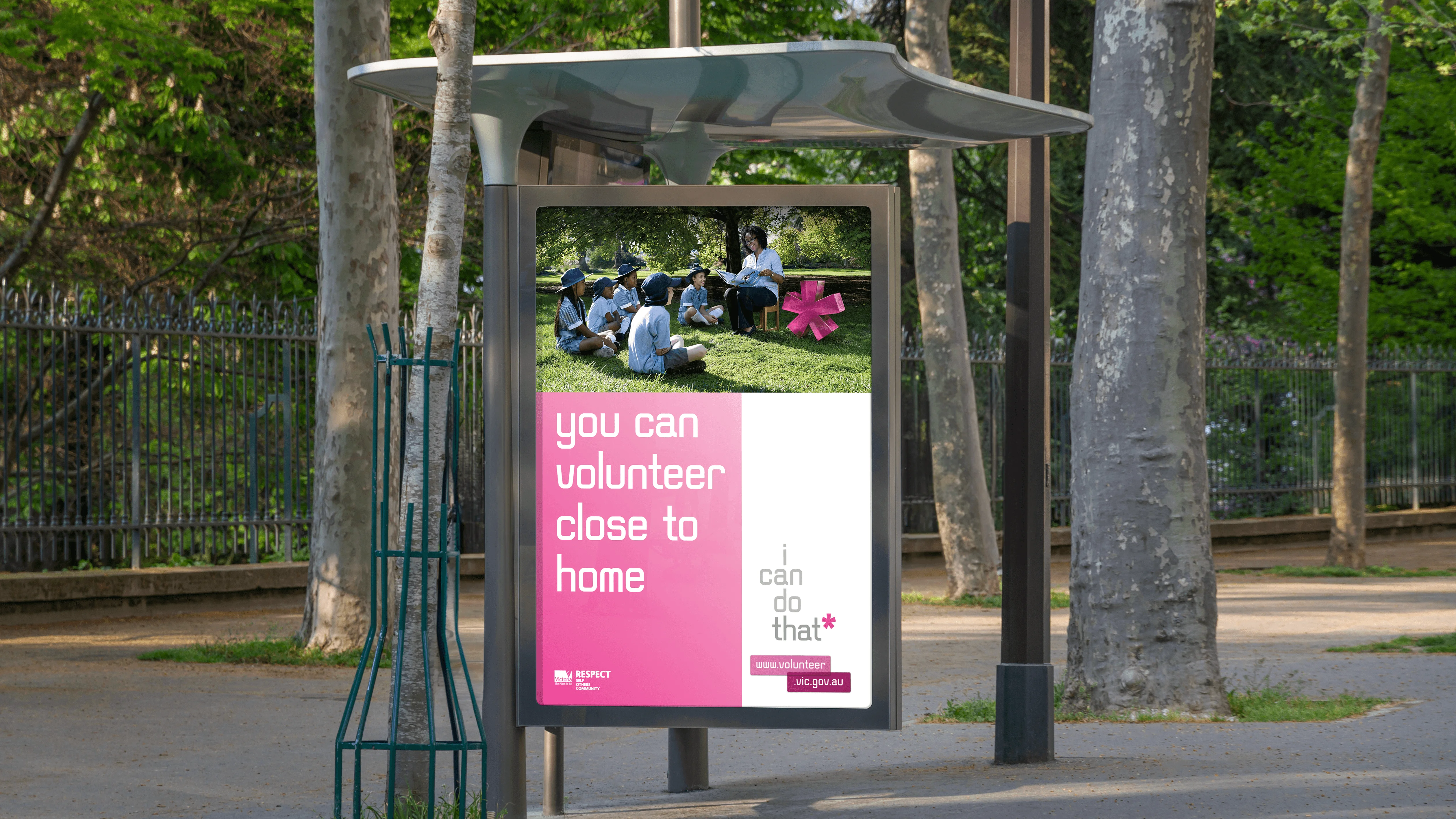 Bus shelter poster 'you can volunteer close to home' with a teacher reading to schoolchildren beside a pink asterisk