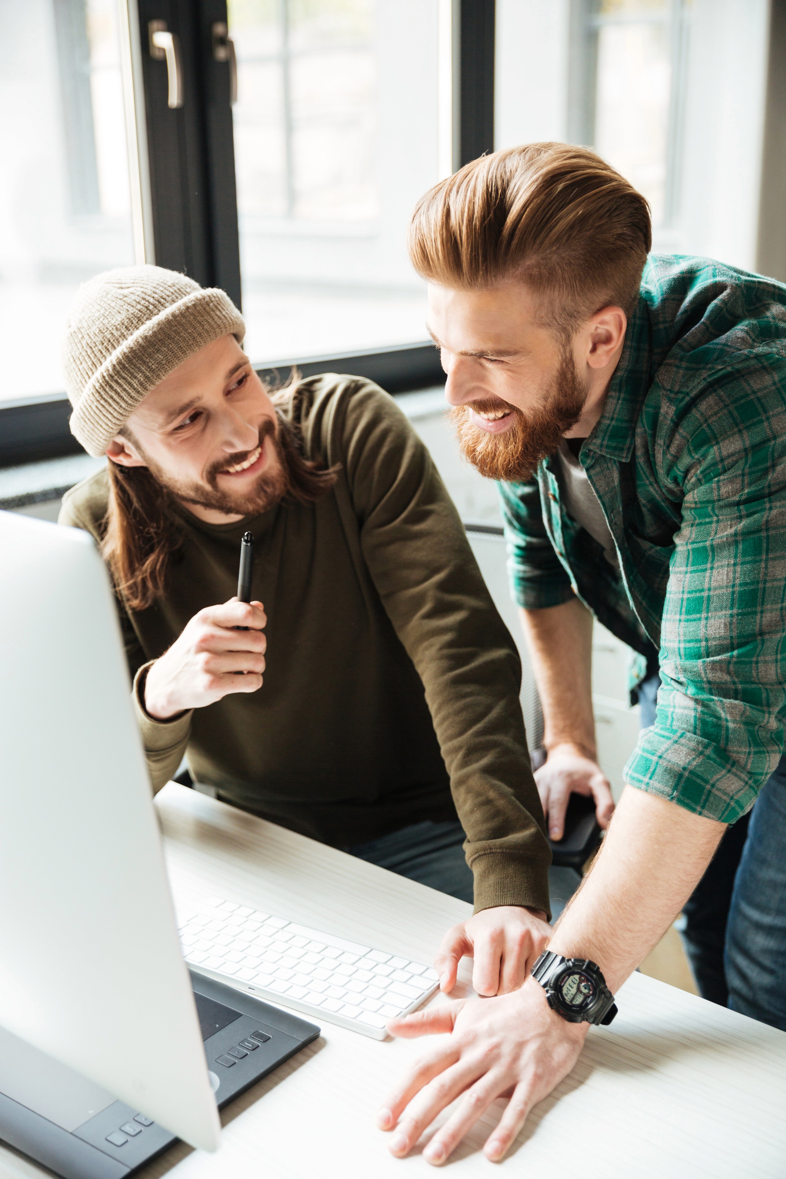 Two young men smiling and collaborating at a computer.