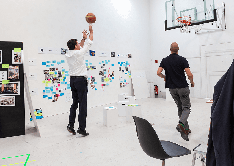 Zwei Personen spielen gemeinsam Basketball in der Halle von DEsign for Human Nature.