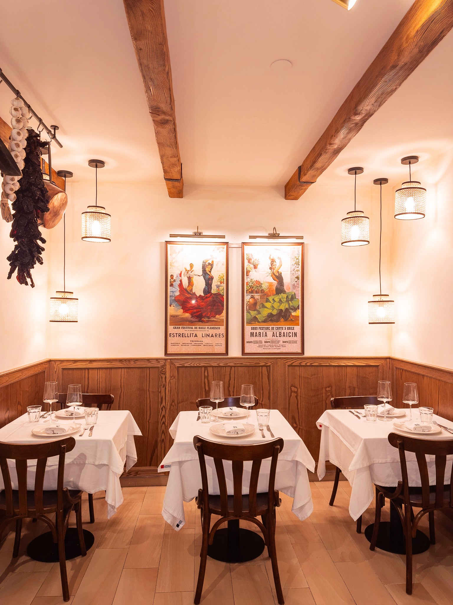 Cozy cafe corner with a round terrazzo table surrounded by wooden chairs, decorated with potted plants and a large mirror reflecting warm light.