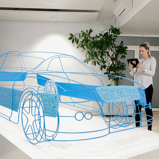 A woman stands in a modern office holding a tablet, examining a large, blue wireframe model of a car displayed on a white table. A potted plant and white walls are visible in the background.