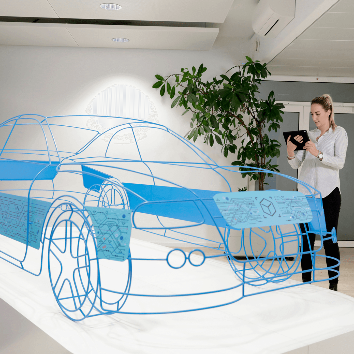 A woman stands in a modern office holding a tablet, examining a large, blue wireframe model of a car displayed on a white table. A potted plant and white walls are visible in the background.