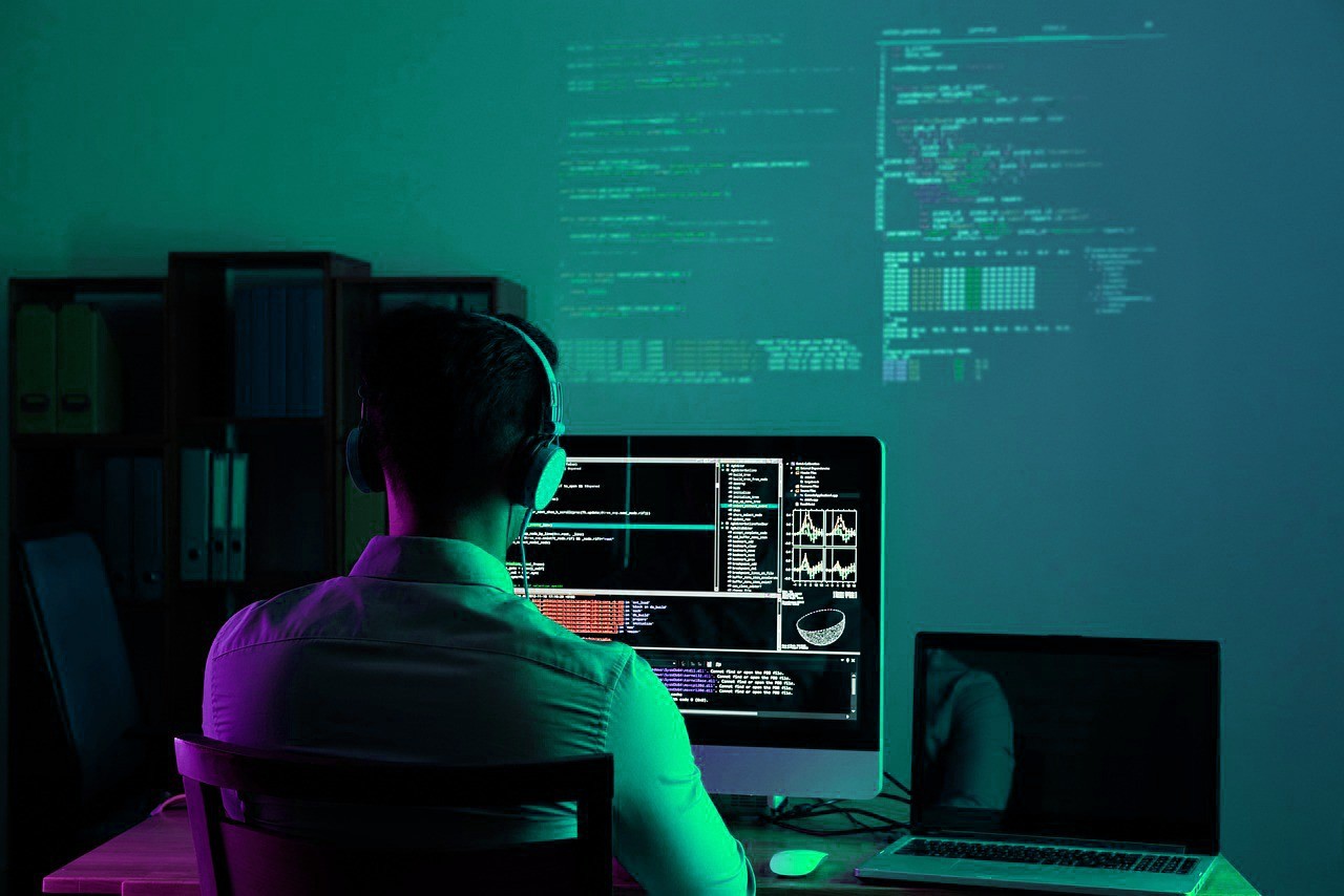 A woman with red hair and a black sleeveless top smiling confidently in a bright, modern indoor setting.