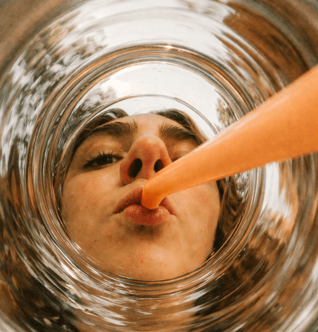 A person’s face hovering above a glass drinking out of an orange straw.