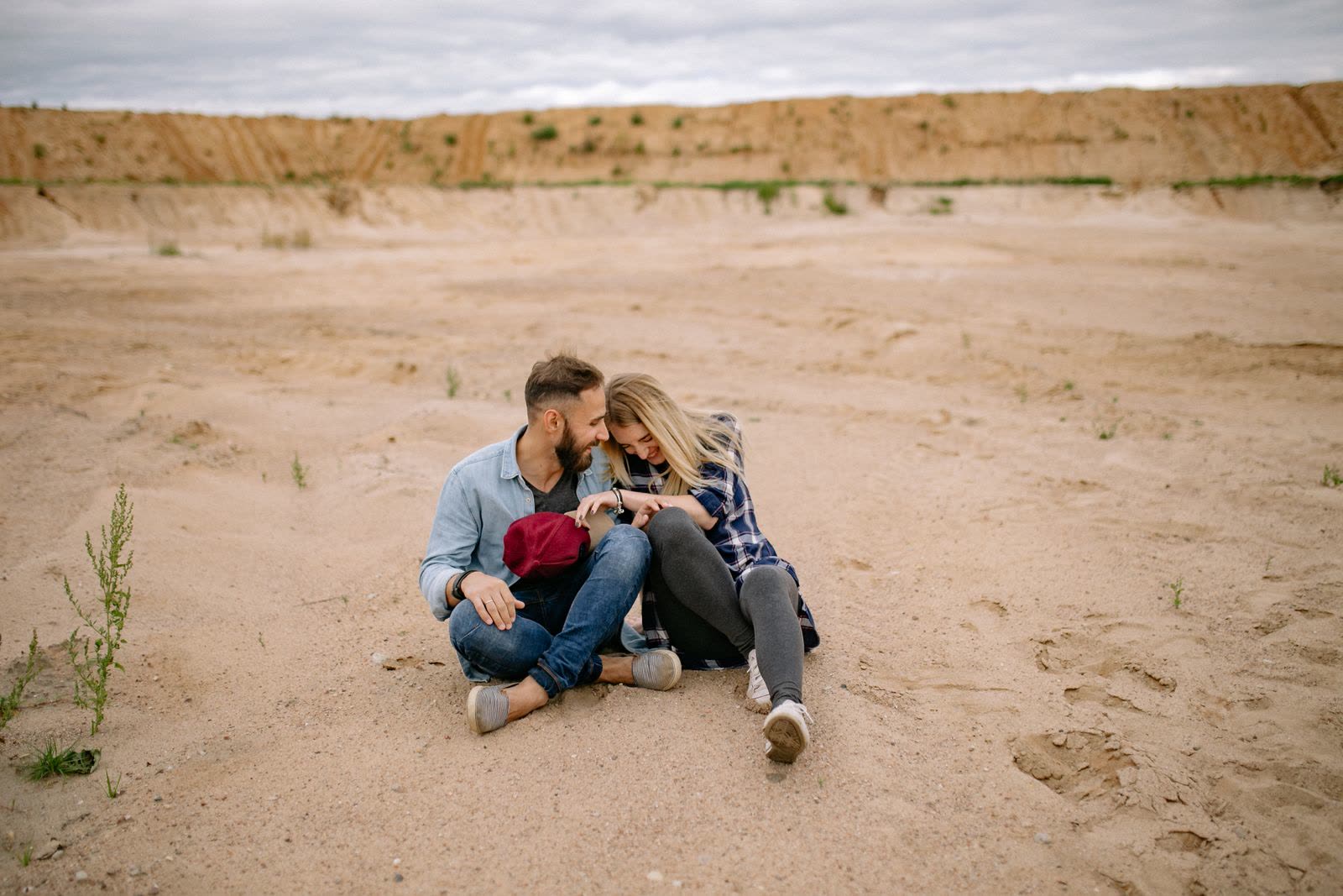 Couple sitting close together on a sand slope under a cloudy sky