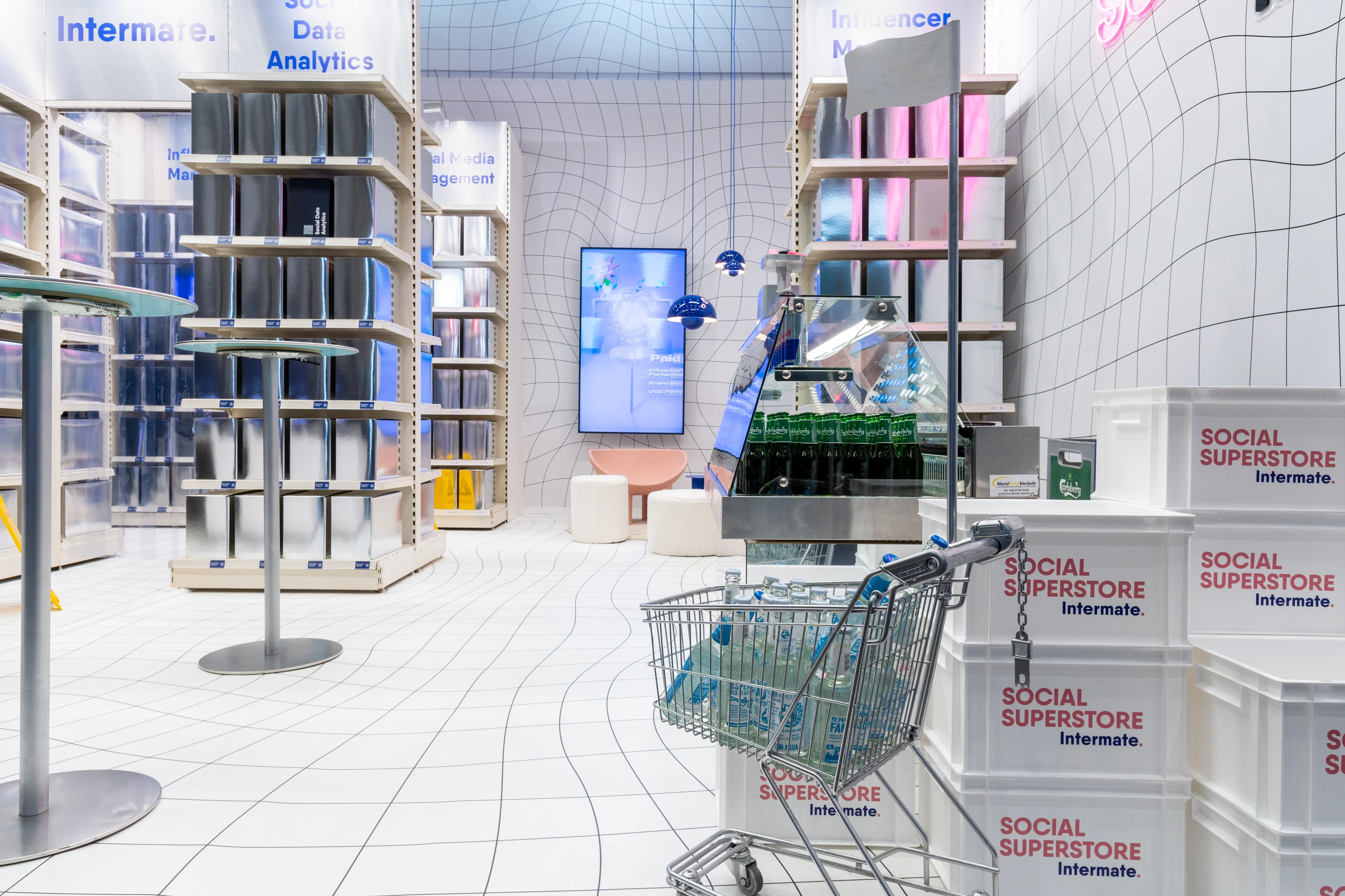 Distorted-grid interior of the Social Superstore with metallic product boxes, drinks station and shopping cart.