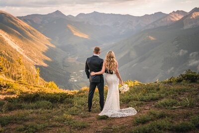 The newlyweds stand arm in arm, looking out over the sunlit valley.