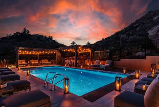 Illuminated swimming pool and lounge chairs beneath a colorful sunset