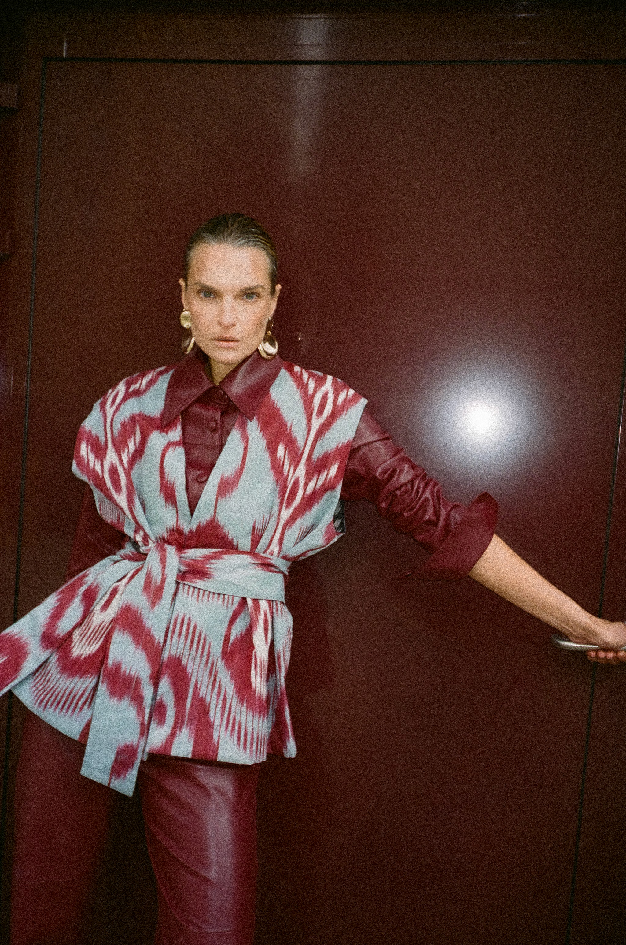 Woman in oversized sunglasses and large earrings walking in an urban setting, wearing a black coat with yellow, white, and blue patterns.