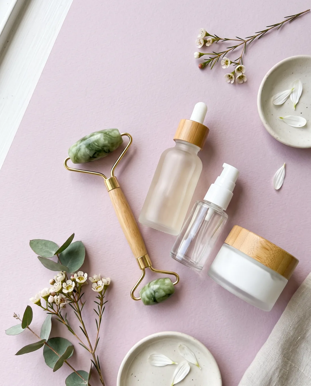Serum bottles and a jade roller on a soft pink surface