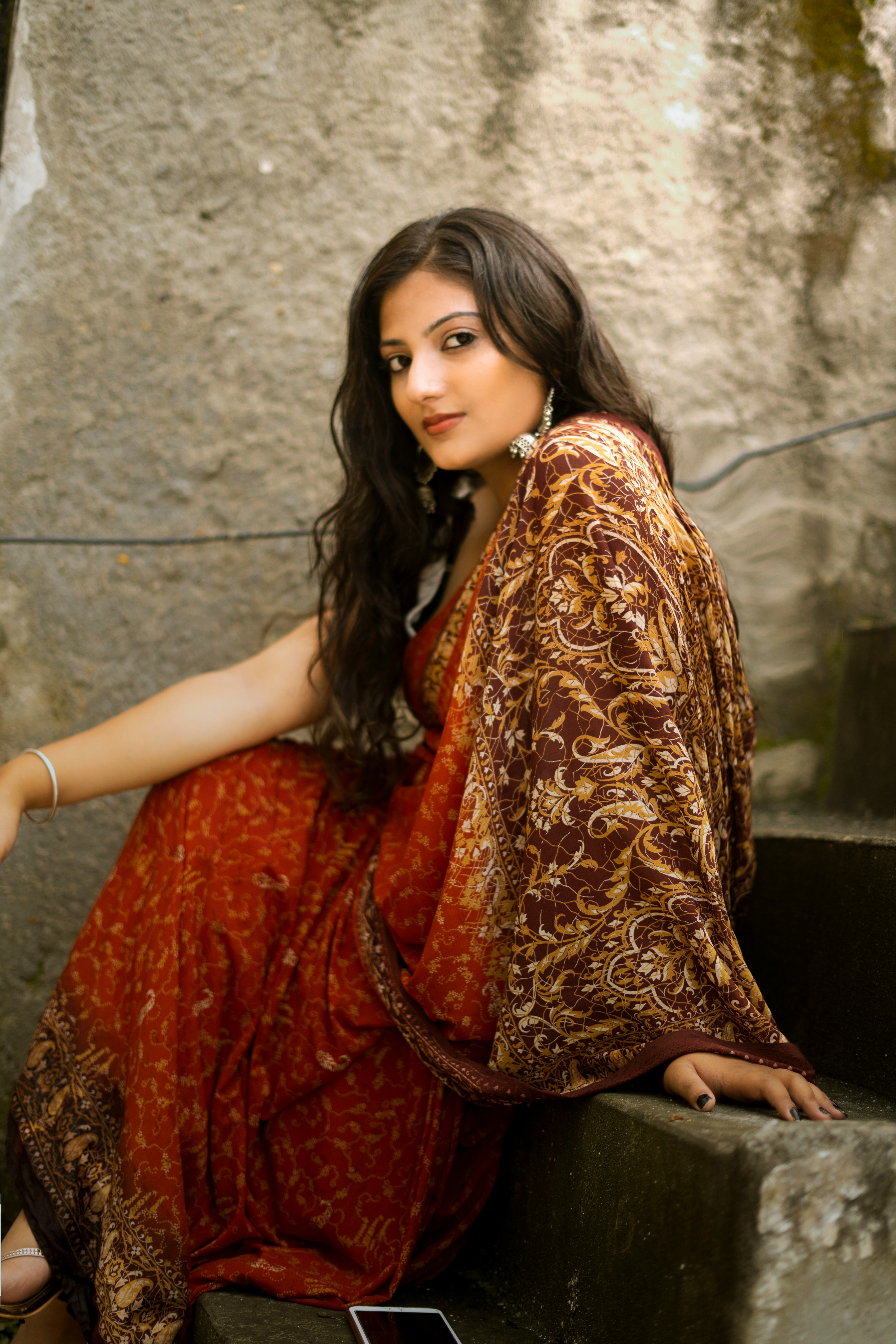 woman in red and gold sari dress sitting on gray concrete stairs