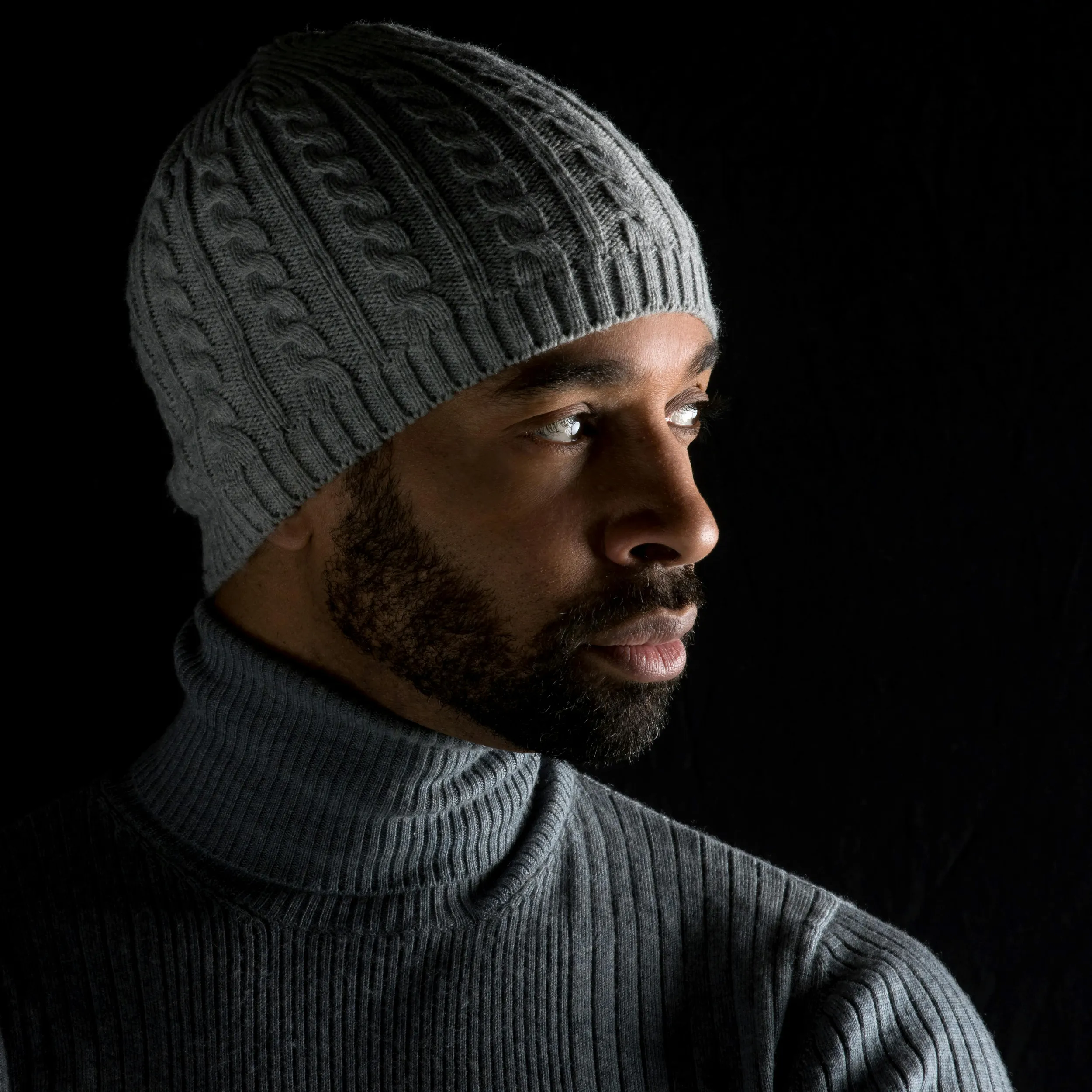 Man wearing knit beanie and turtleneck sweater, low-light fashion portrait