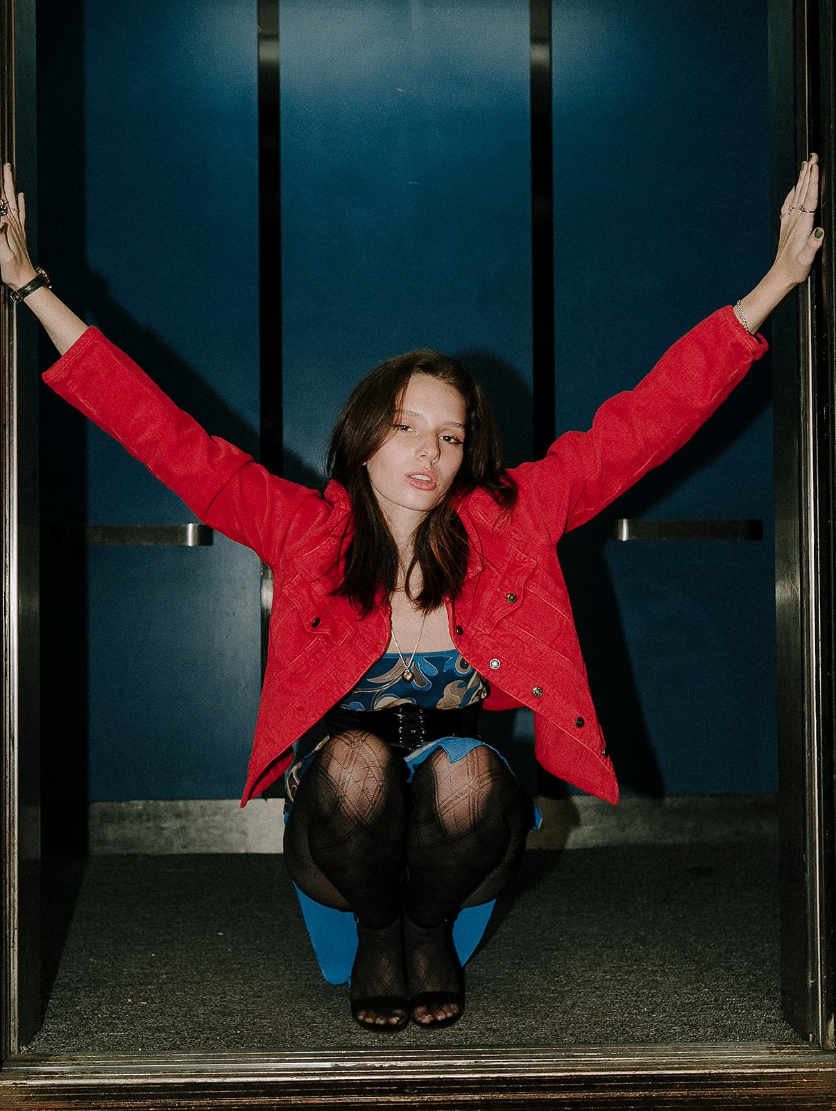 Model crouching in an open elevator wearing a red jacket at Revelator Studio’s photography studio in Shreveport.