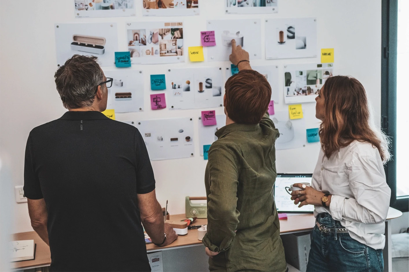 Trois designers observant et discutant un mur d’inspiration rempli de visuels, de croquis et de post-its colorés lors d’une session créative. Numa Rousseau et Vivien Durisotti
