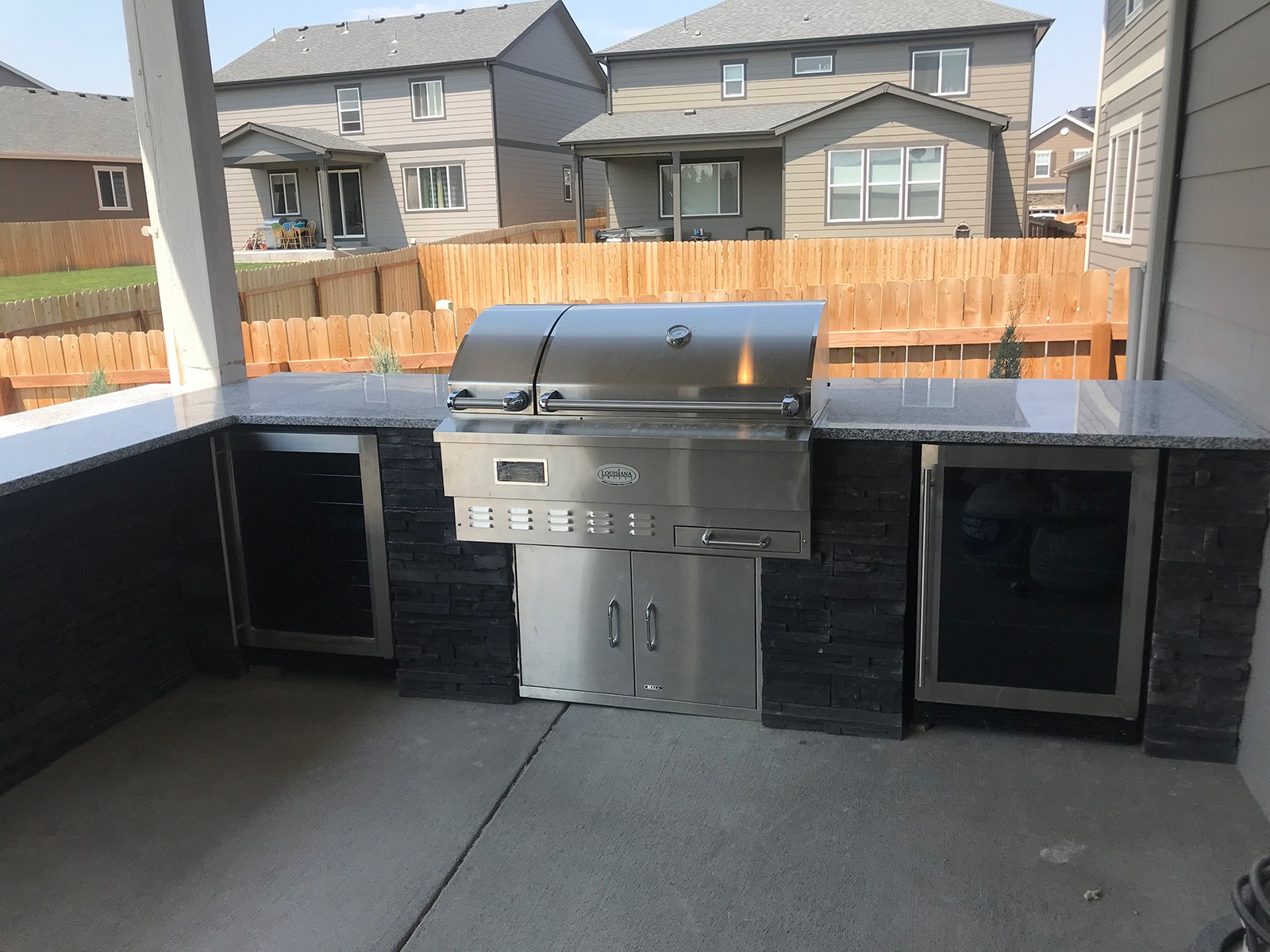 stainless steel grill with an outdoor kitchen in the backyard surrounded by other houses, a large black stone wall behind it