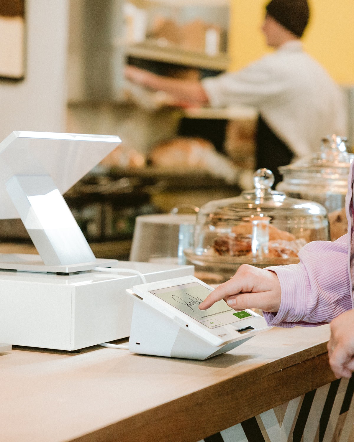 Customer in a coffee shop completing a transaction by signing their name with their pointer finger on a Mini device.
