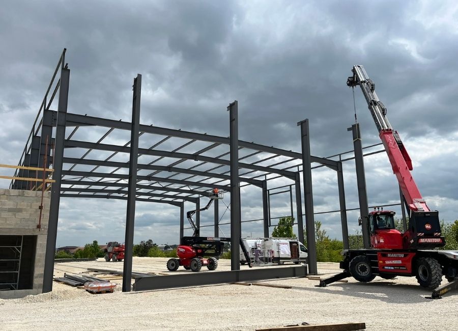 Structure métallique verticale d’un bâtiment en cours d’assemblage avec grue visible.