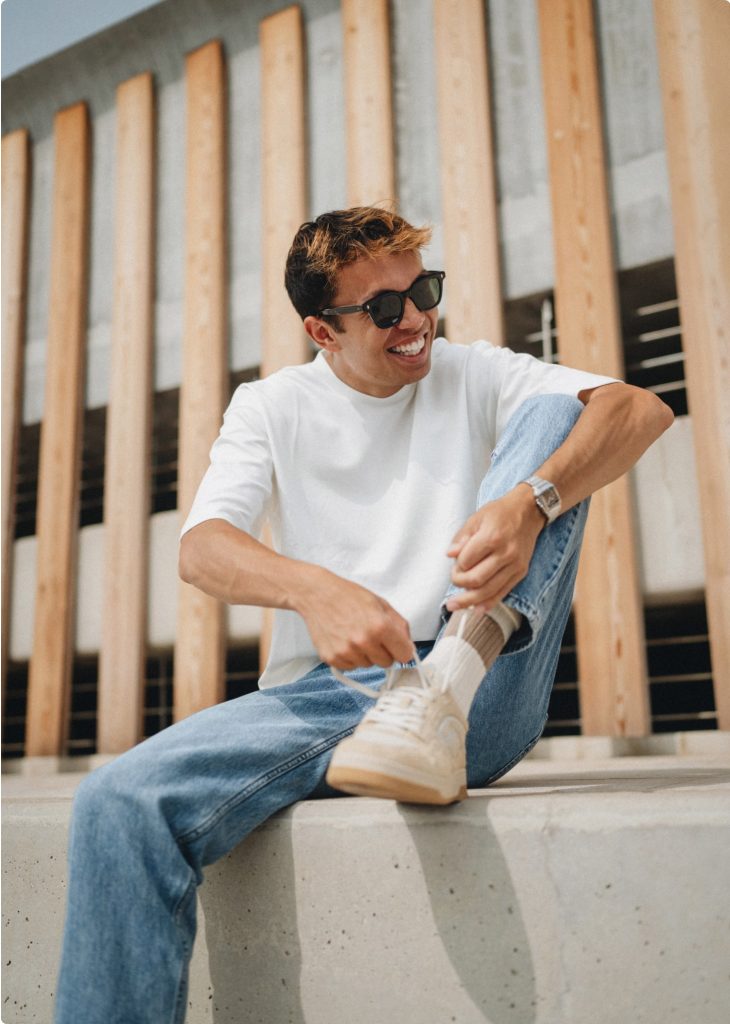 Lifestyle-Foto für den Alex-Albon-Webshop von Flatline: Mann in weißem Shirt und Jeans bindet seinen Sneaker