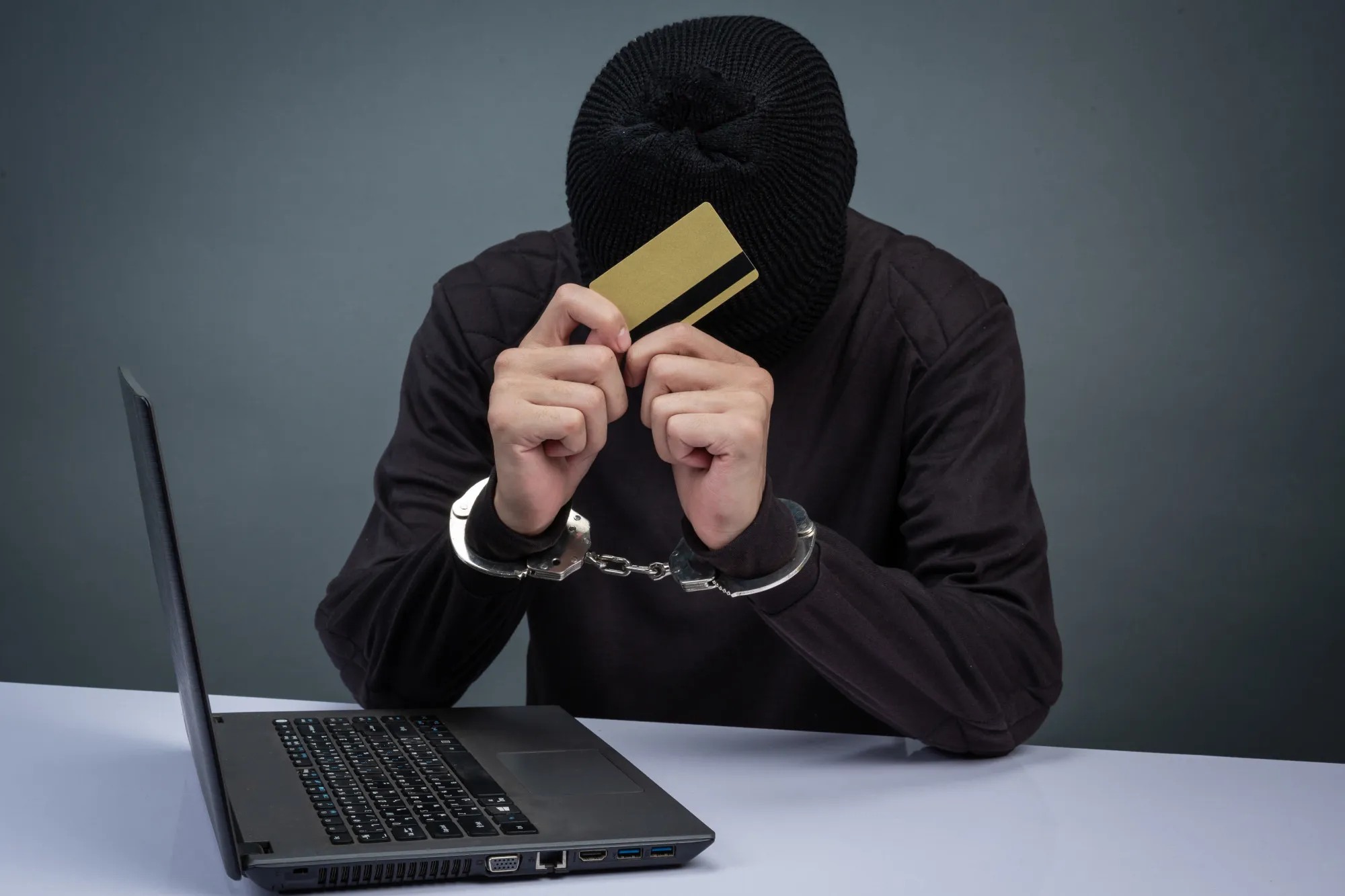 A handcuffed cybercriminal in a mask holds a credit card, symbolizing the "organized crime" TikTok Shop is fighting.