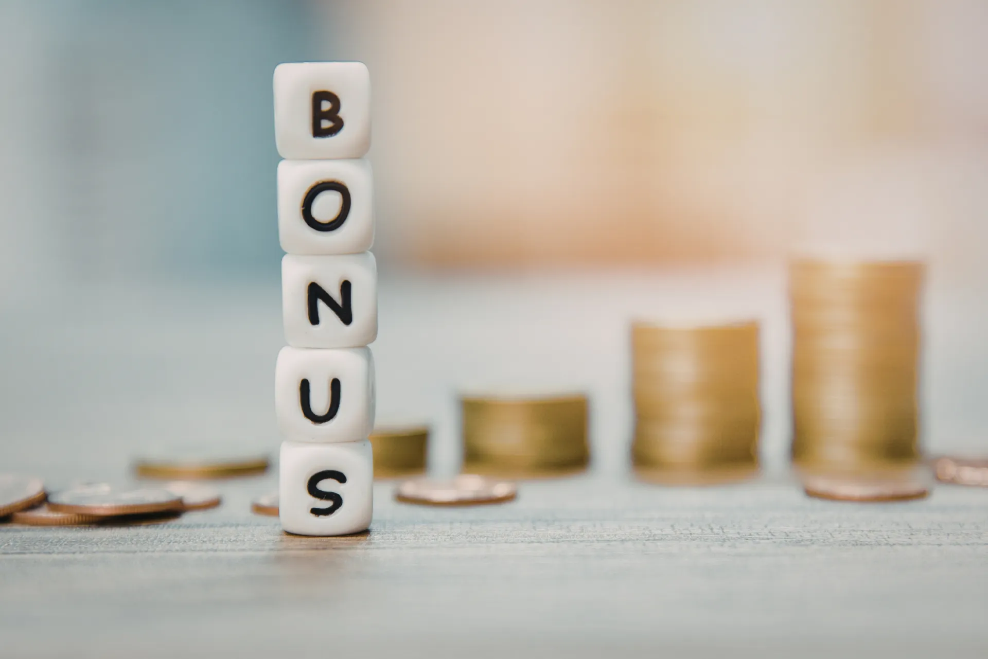 Ein Geldstapel im Hintergrund, welcher hinter Würfeln steht. Die Würfel zeigen vertikal das Wort "Bonus".