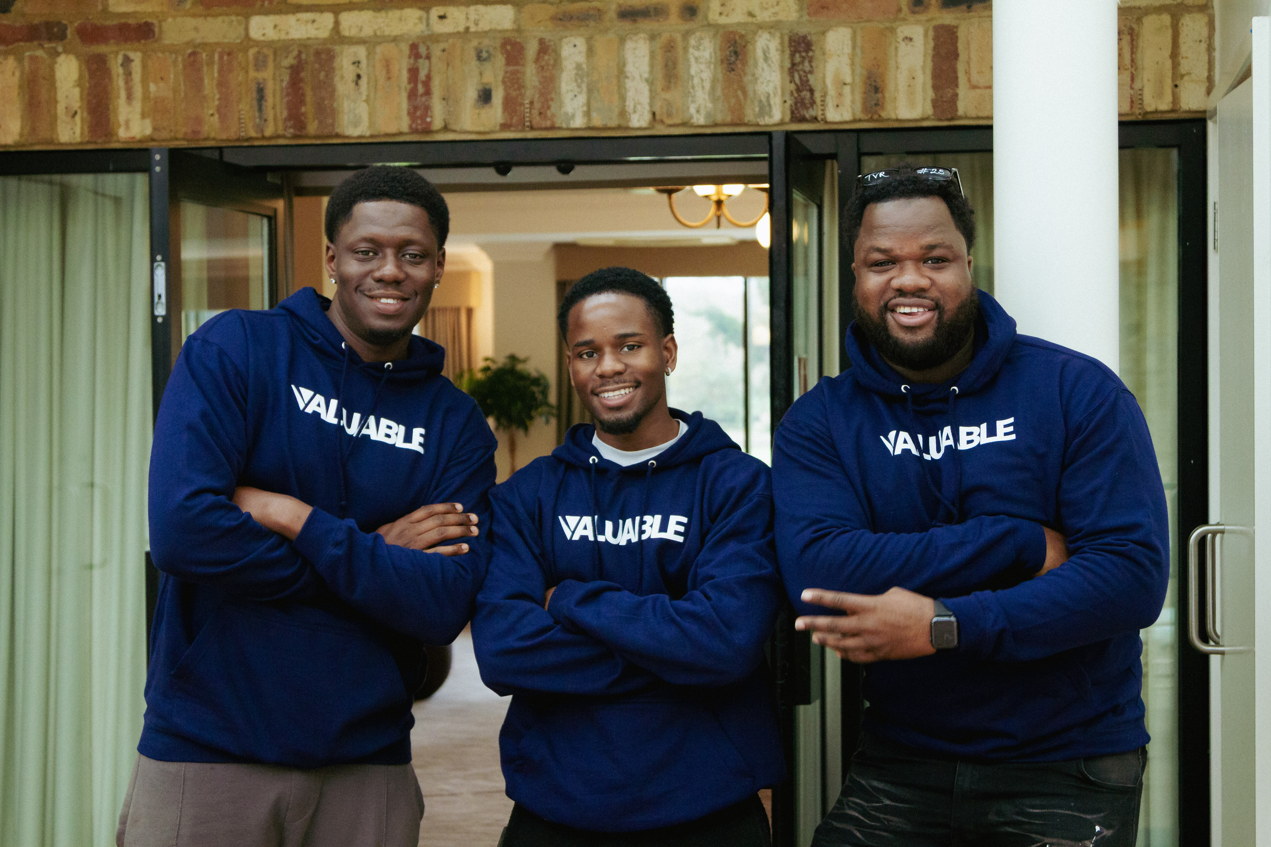 Three valuable community members stand together smiling, wearing matching navy blue Valuable sweatshirts. 