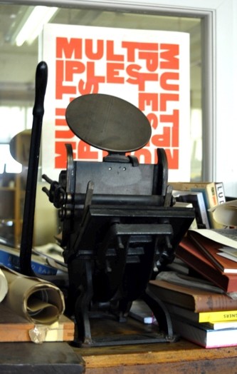 A photo of a machine that looks like a hand printing press near a stack of books.