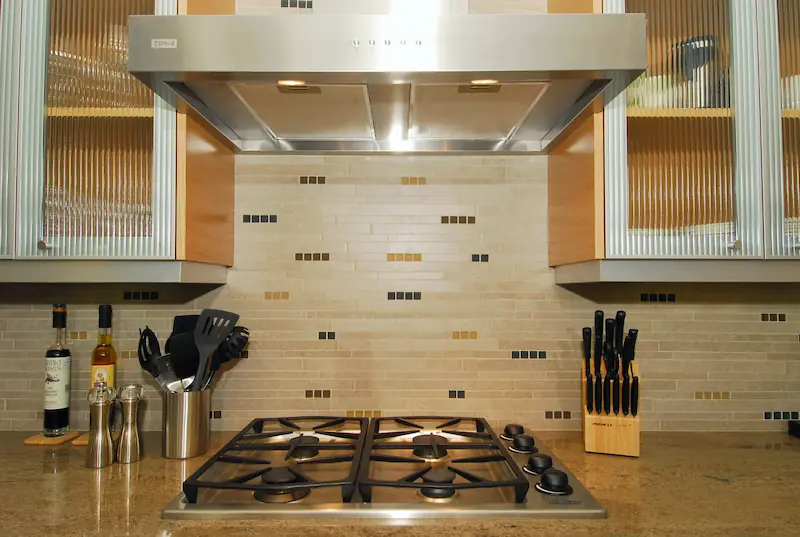 Modern kitchen backsplash with stainless steel hood. Modern kitchen with wooden cabinetry, stainless steel appliances, and granite countertops. Irvine Transitional Modern. Photo by Chris Darnall.