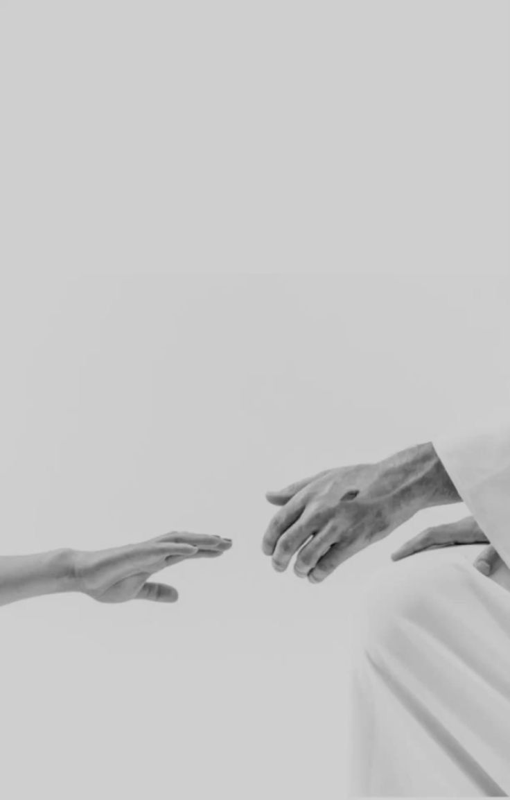 A person with long hair stands against a bright, hazy background, reaching out with one hand.