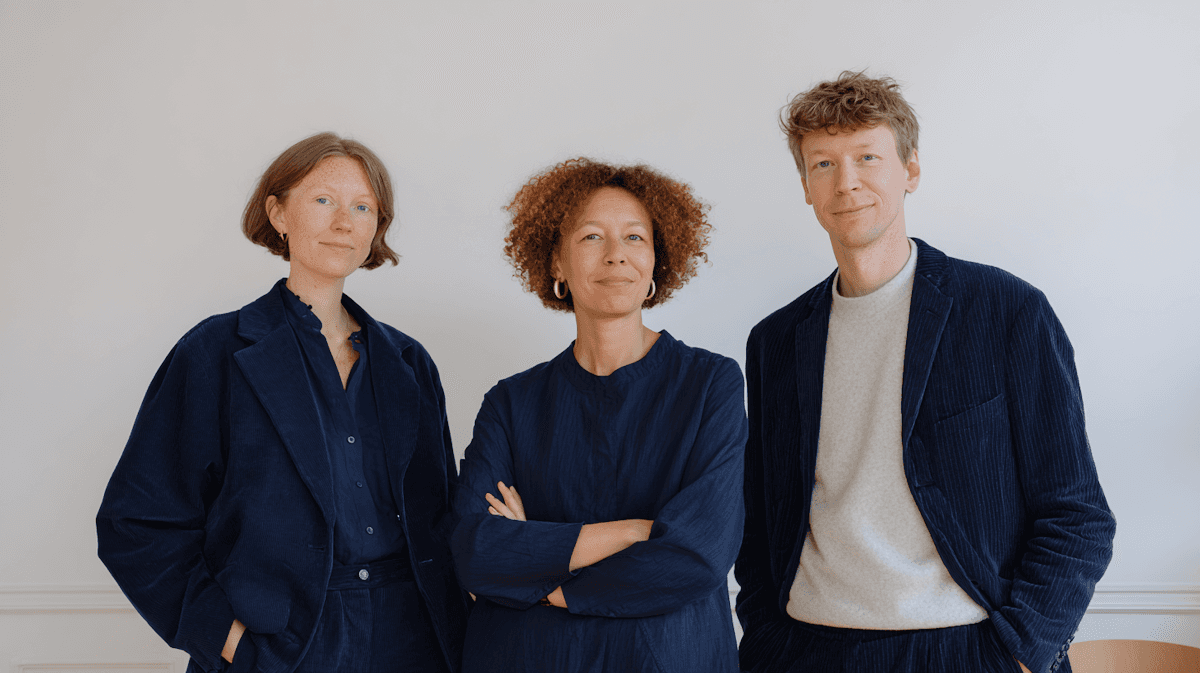 Profile view of a man working on a laptop at a desk with a small tree and artistic shadows on the wall.