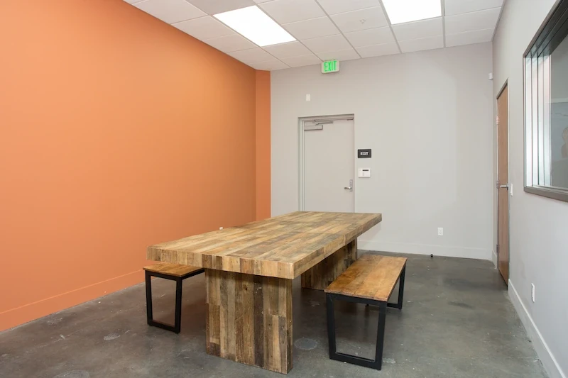 Minimalist meeting room with wooden table, benches, and orange accent wall at Kannabis Works.