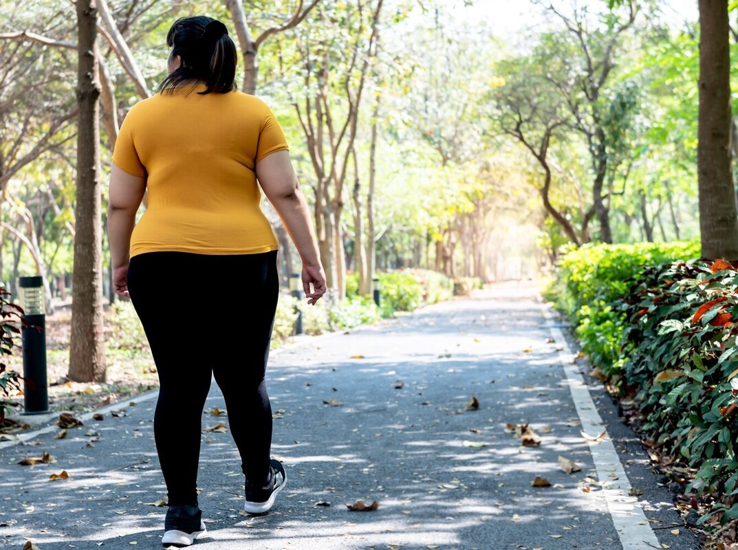 overweight woman going for a light walk outside with beautiful trees as part of the best workout routine to lose weight