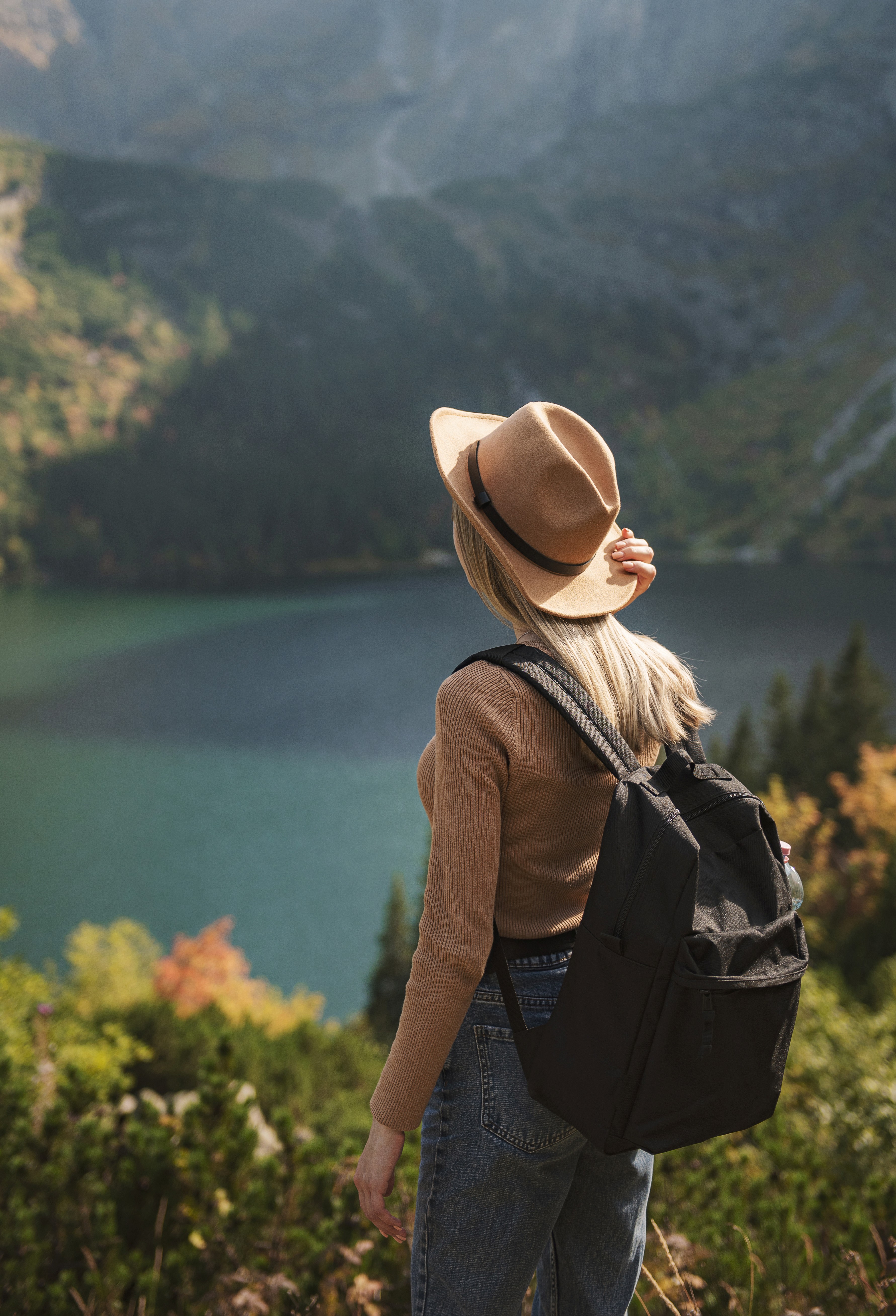 A smiling woman with her arms crossed, standing against a dark green background. She has long, dark hair.