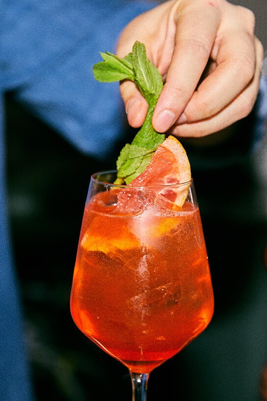 Hand decorating a grapefruit spritz with some mint