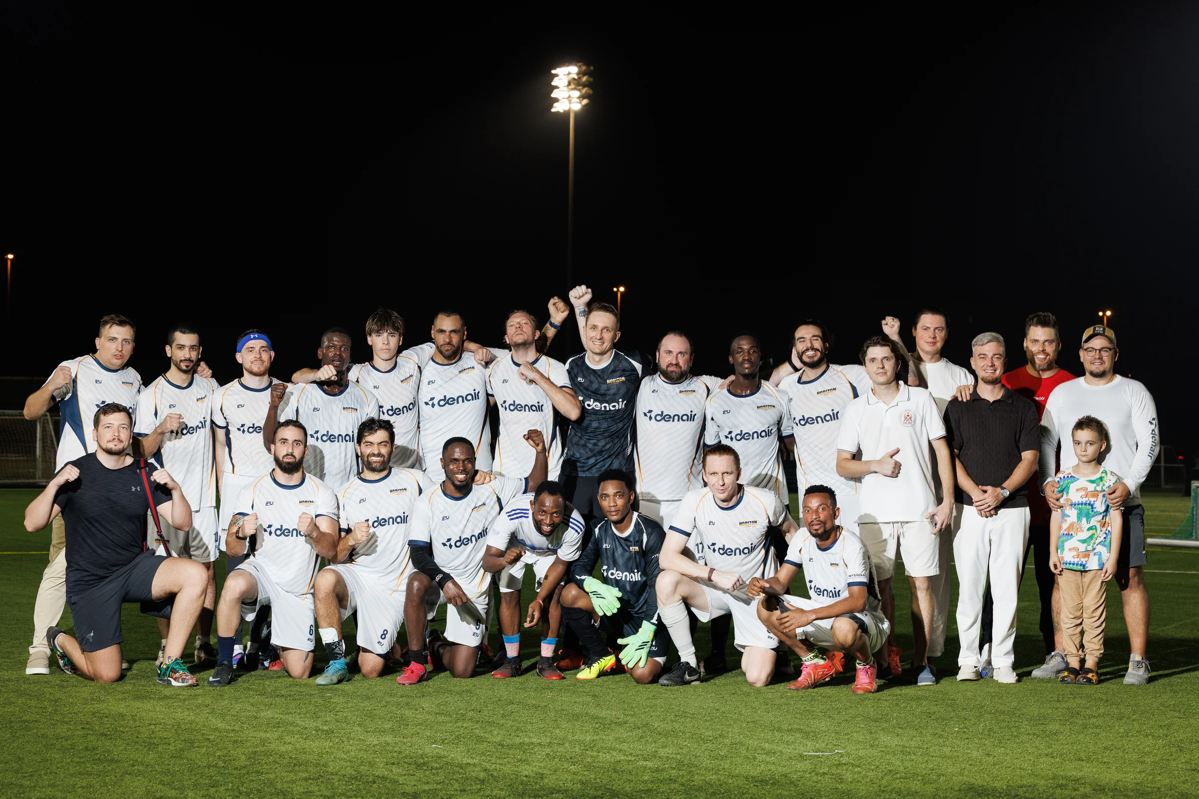 Horizon FC group posing on a floodlit football pitch, with DENAIR branding visible on white and dark team shirts.