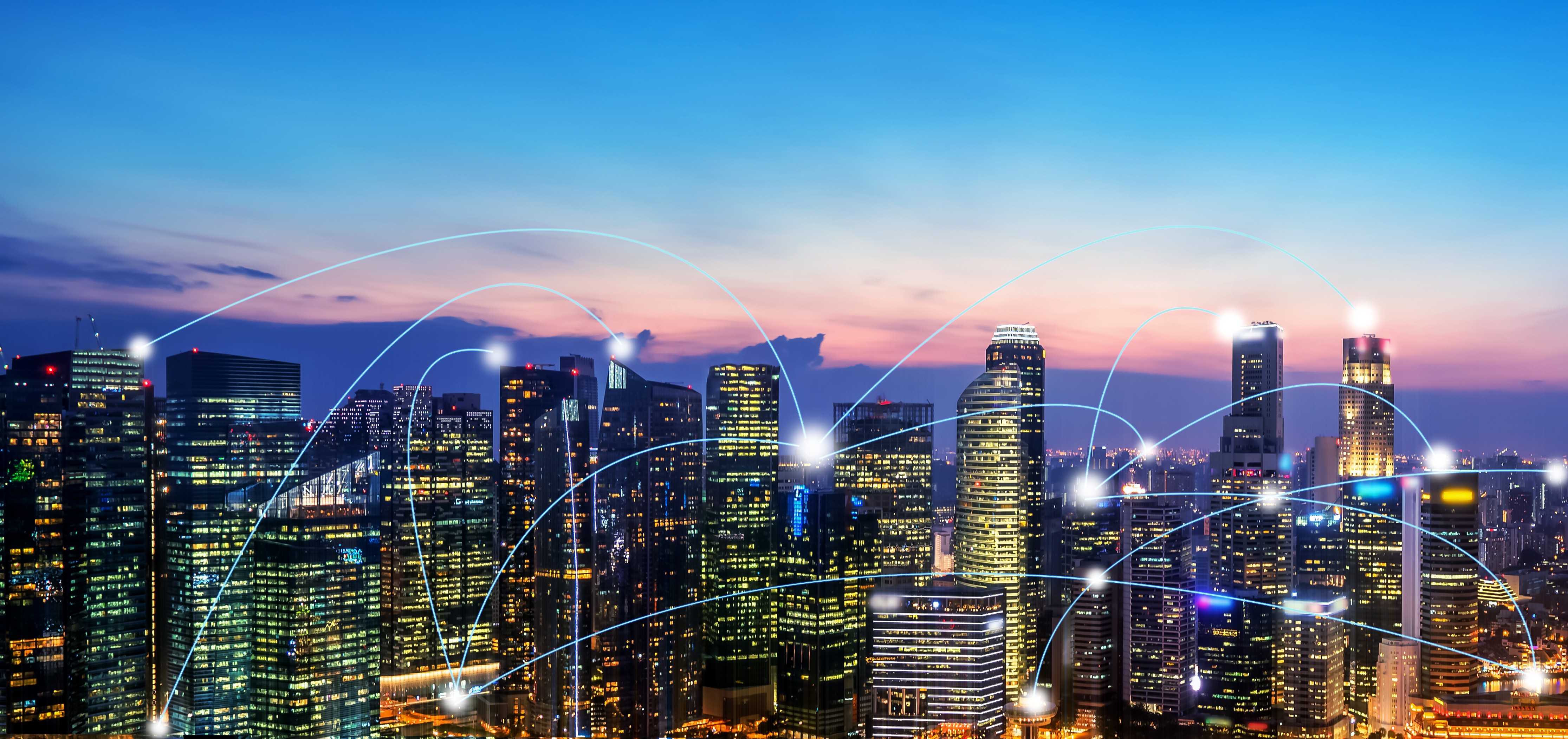 Cinematic image of city scape skyscrapers with yellow lights against a sunset background in blue and pink