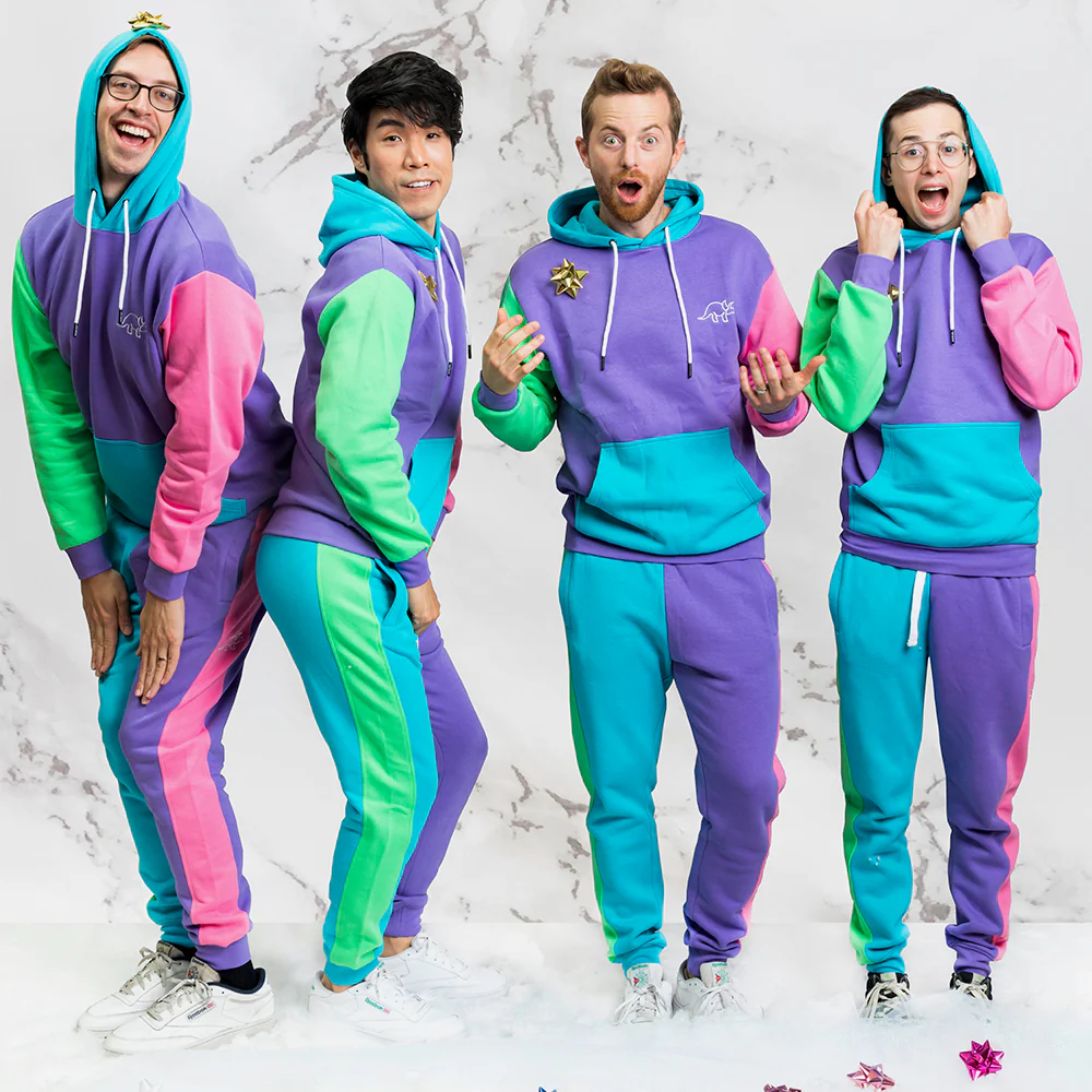 Four people pose together, wearing brightly colored, retro-style outfits in shades of purple, green, and pink.