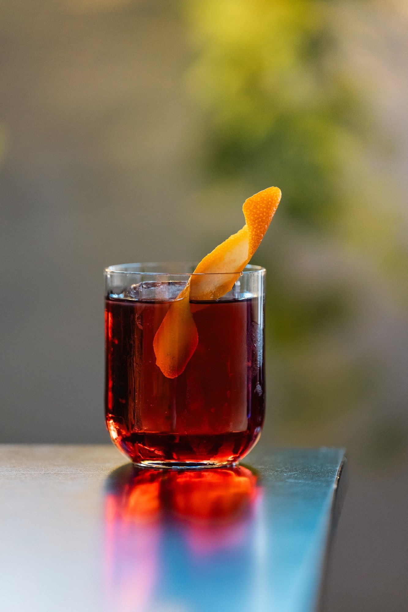 Cocktail rosso scuro in tumbler con guarnizione scorza arancia, su tavolo nero