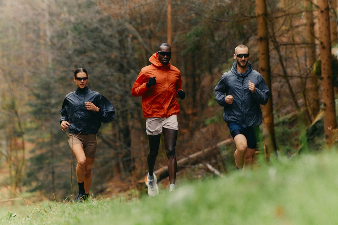 Three mountain runners in mid-stride, racing along a rugged ridge with focused expressions.