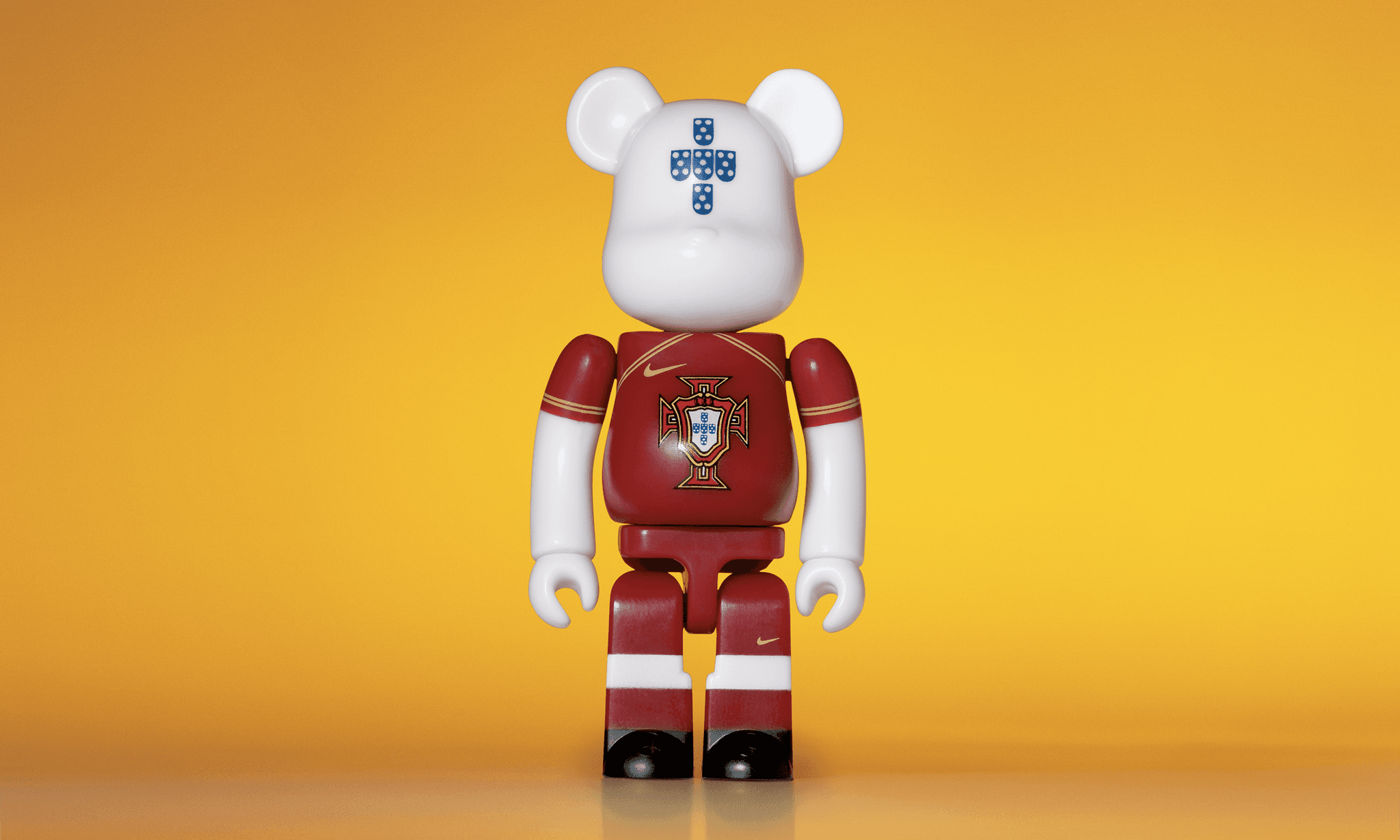 A single 3.5” tall Bre@rbrick/Nike toy created to commemorate the 2006 Portuguese World Cup football team. The toy is painted to appear in the Portuguese football kit and stands in the center of the frame in front of a bright yellow background.