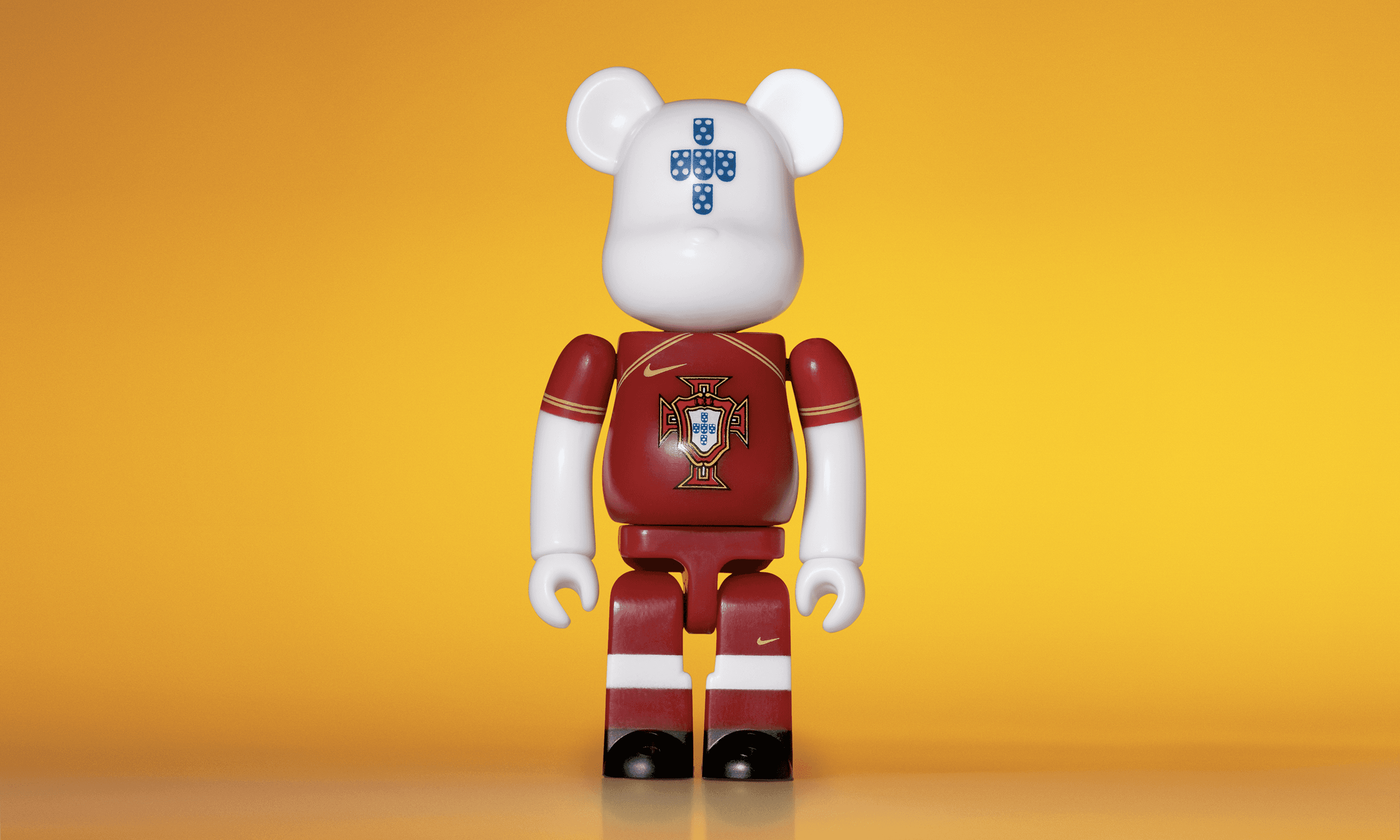 A single 3.5” tall Bre@rbrick/Nike toy created to commemorate the 2006 Portuguese World Cup football team. The toy is painted to appear in the Portuguese football kit and stands in the center of the frame in front of a bright yellow background. 