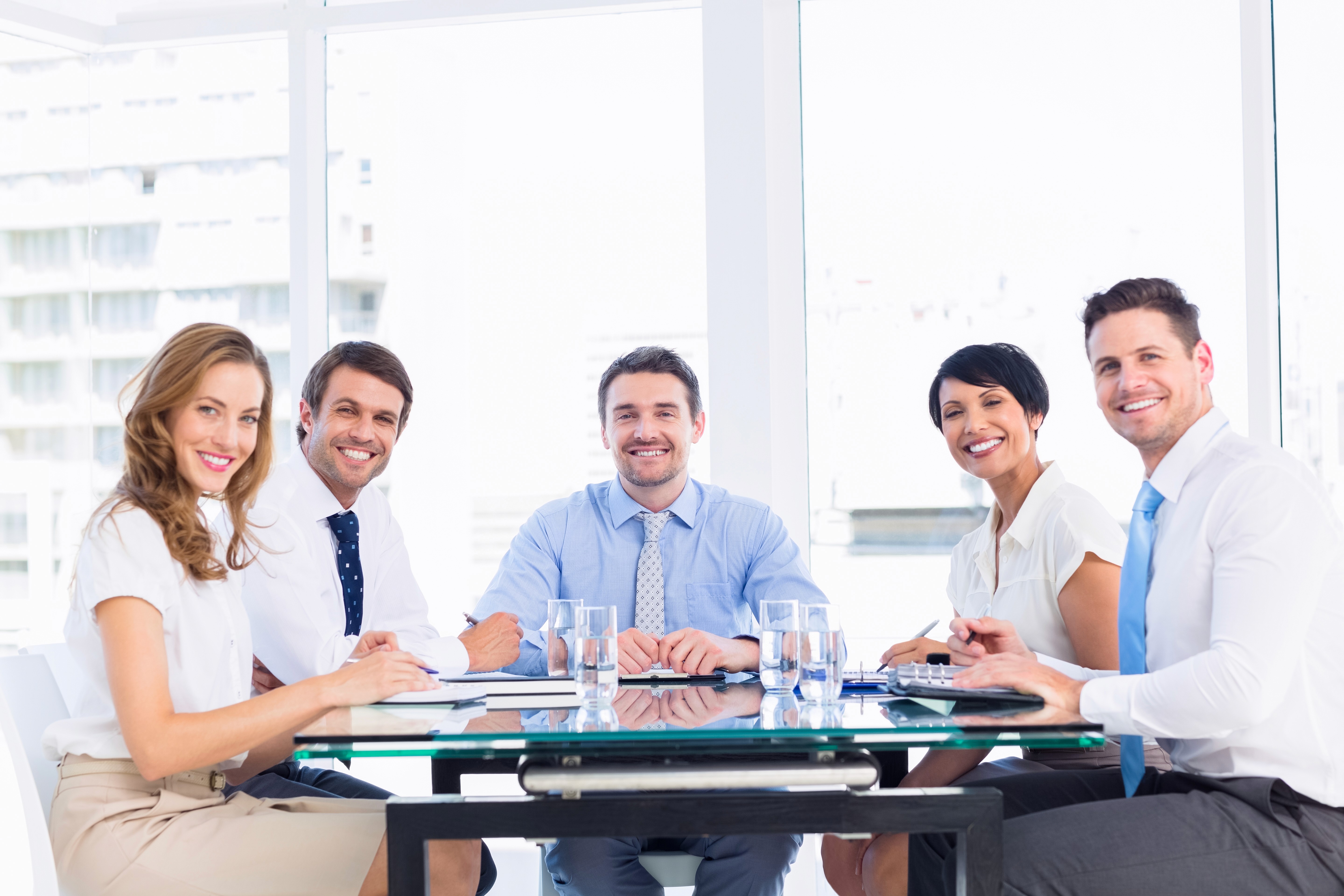 A blonde woman smiling and holding a tablet during a meeting, with colleagues engaged in reviewing documents around her